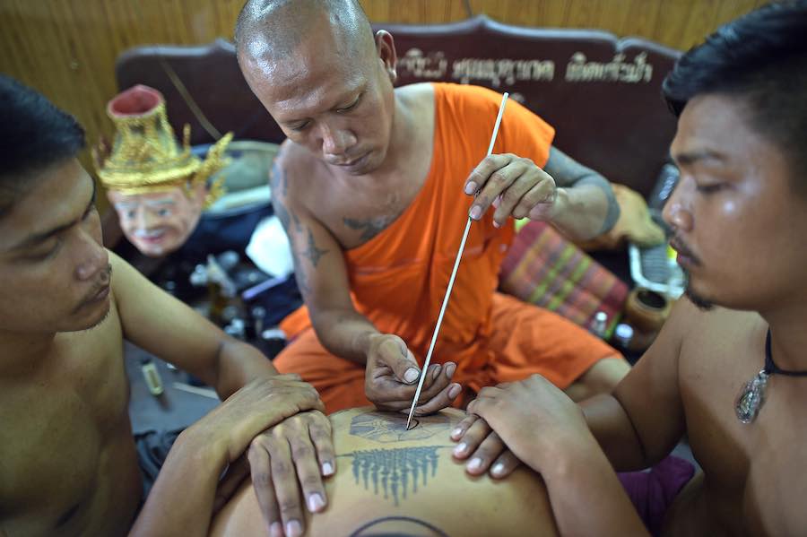 A master monk giving a Sak Yant tattoo in an authentic temple in Thailand, assisted by two helpers